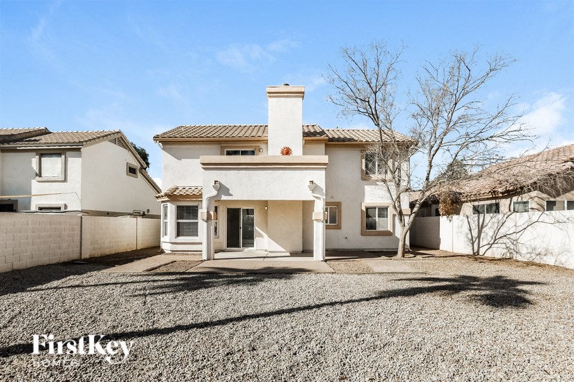 A white house with a brown roof and a chimney is surrounded by a gravel driveway.