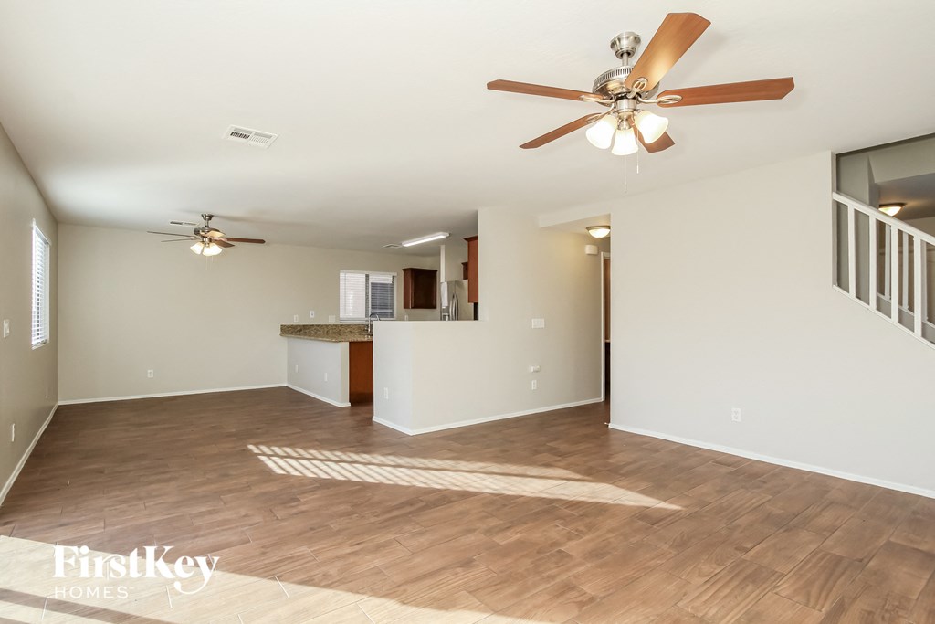 an empty living room with a ceiling fan and a kitchen