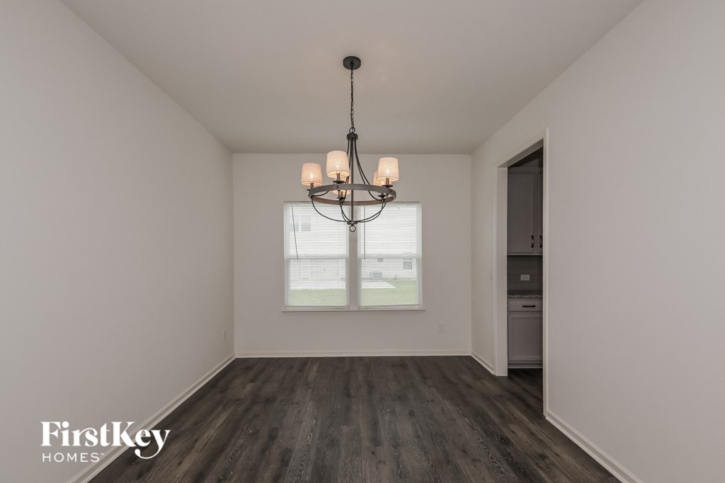 A chandelier hangs in a well-lit, empty room with a window and a door.