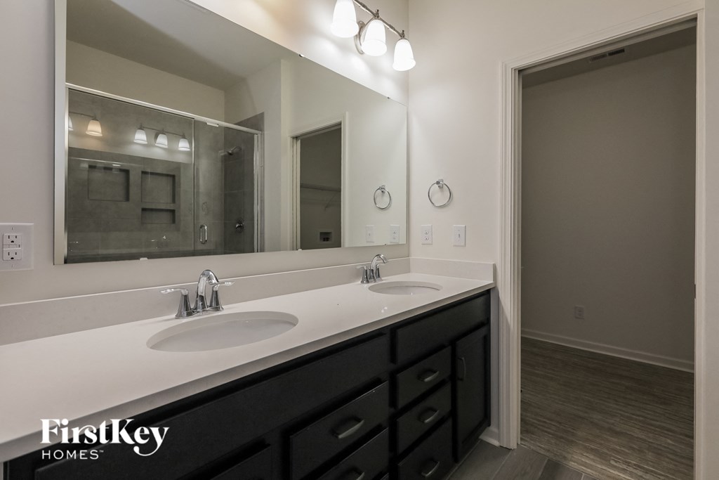 A bathroom with a large mirror, two sinks, and a wooden floor.