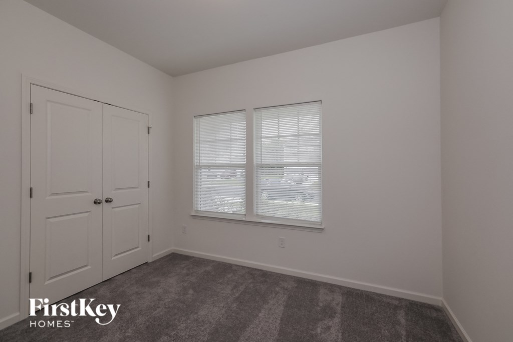 A room with a carpeted floor, a window with blinds, and a door.