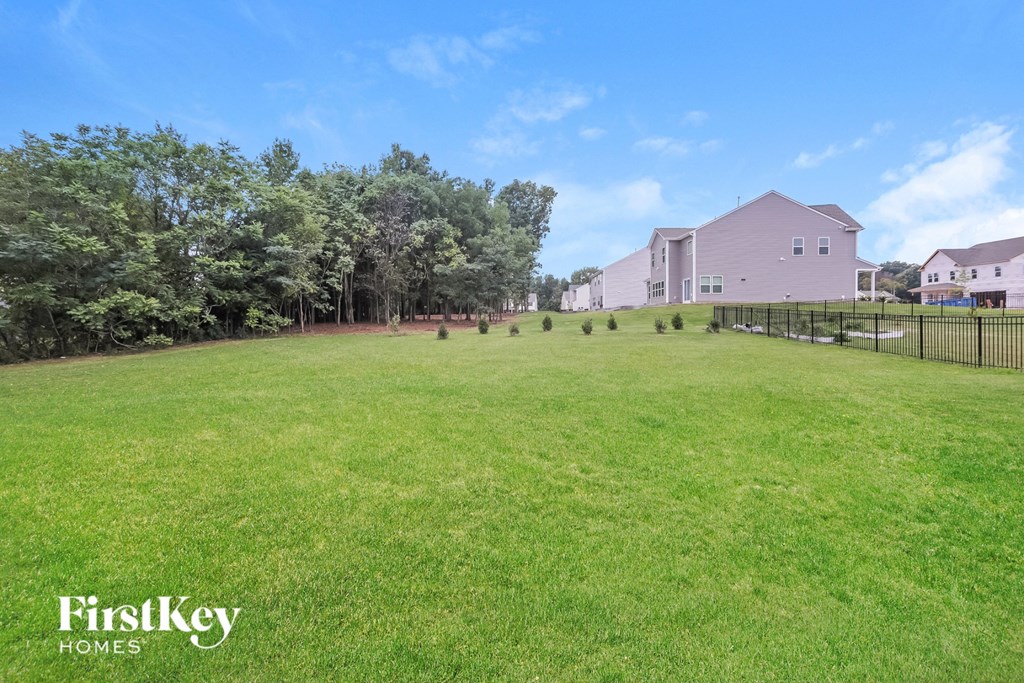 A grassy field with trees and a house in the background.