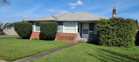 A house with a grey roof and a grey door is surrounded by green grass.