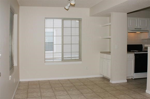 an empty living room with a kitchen and a window