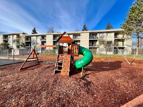 A playground with a green slide and a brown wooden structure.