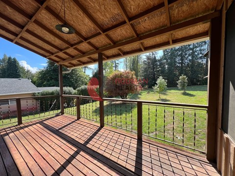 A wooden deck with a railing and a view of a green lawn and trees.