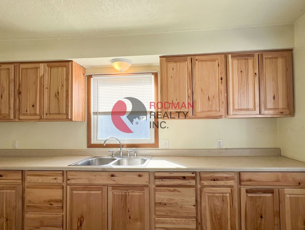 A kitchen with wooden cabinets and a window with blinds.