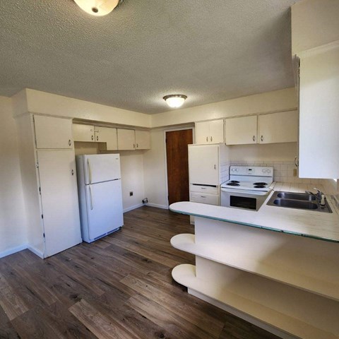 A kitchen with a white fridge and wooden floors.
