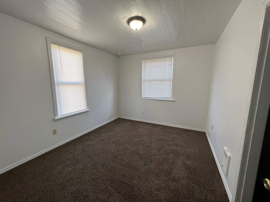 an empty room with carpet and two windows