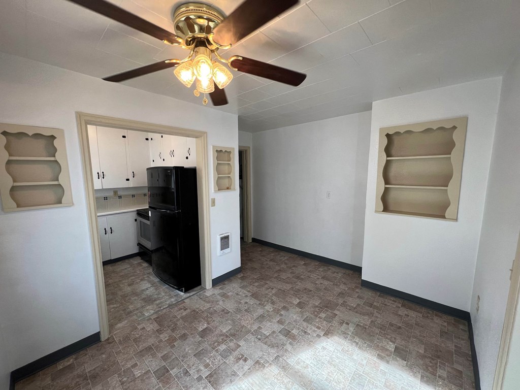 an empty living room with a ceiling fan and a kitchen