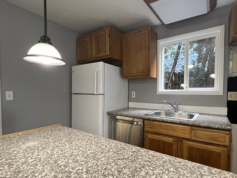 A kitchen with a white refrigerator and a window with a view of trees outside.