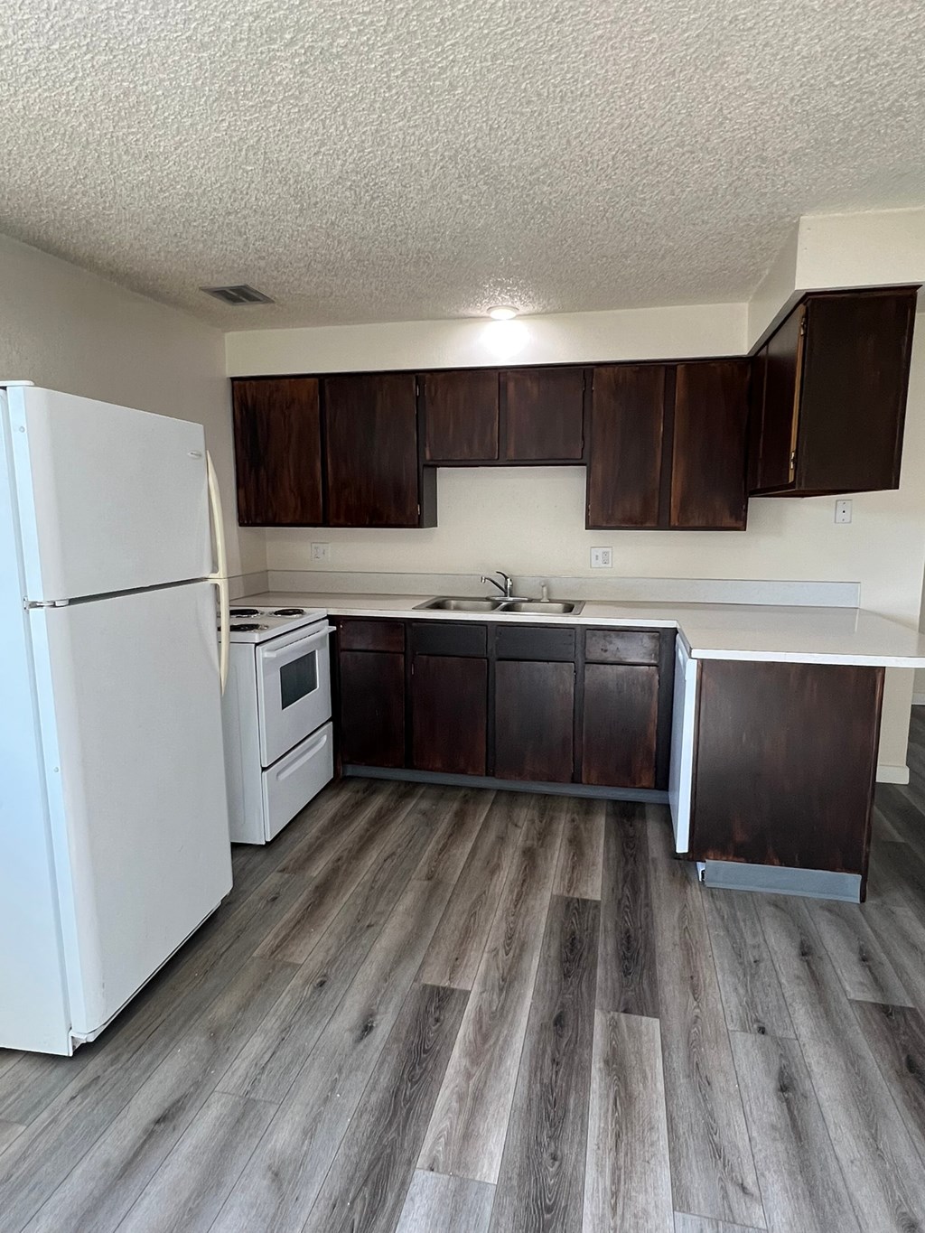 A kitchen with a white fridge and wooden floors.