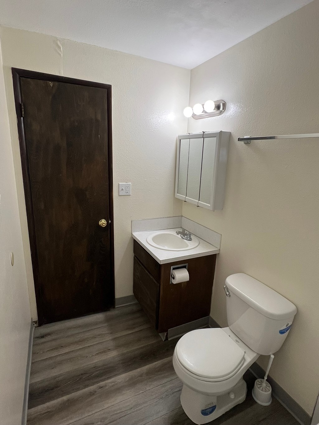 A white toilet with a blue sticker on the side is in a bathroom with a wooden door.