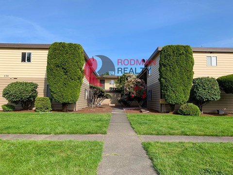 A building with a sign that says "Rodman Realty" is surrounded by green bushes and trees.