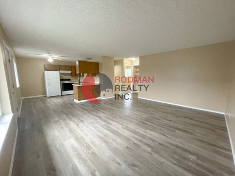 A spacious room with wooden flooring and a large window on the left side.