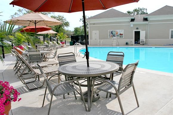 a patio table with chairs and umbrellas next to a pool