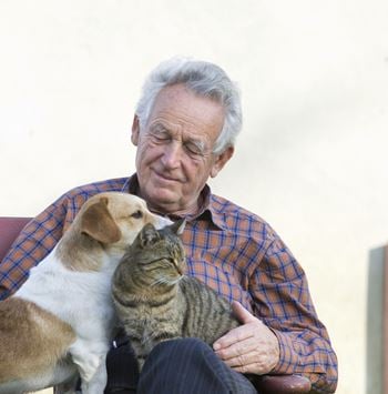 Elderly man holding dog and cat