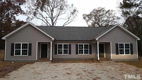a small gray house with a driveway and some trees