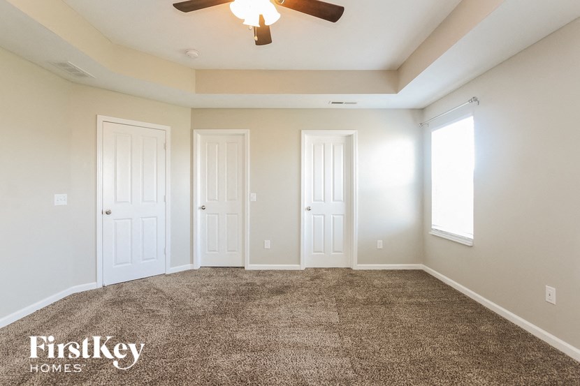 a carpeted living room with two doors and a ceiling fan
