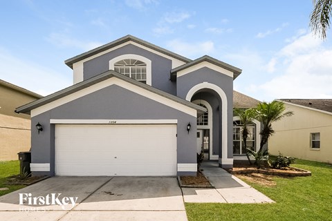 A grey house with a white garage door and a black trash can.