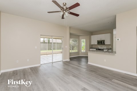 A spacious living room with a ceiling fan and a kitchen area in the background.
