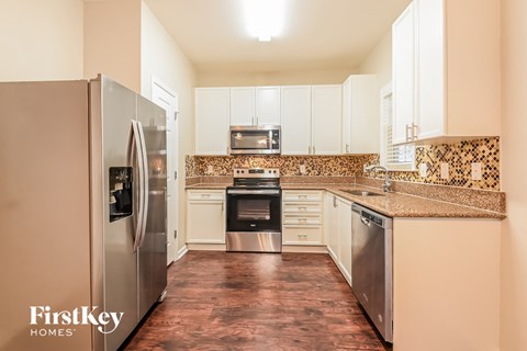 A kitchen with a refrigerator on the left and a stove top oven in the middle.