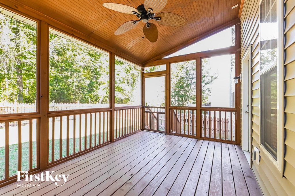 A wooden deck with a ceiling fan and a view of trees.