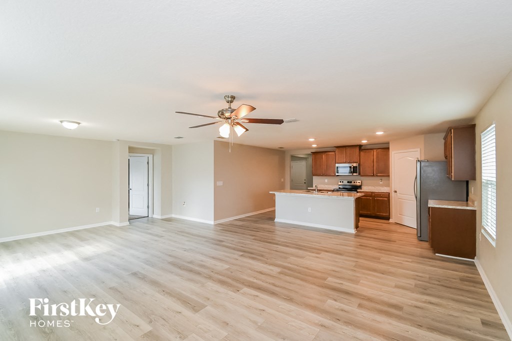 an empty living room with a kitchen and a ceiling fan