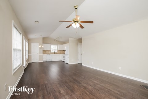 an empty living room with a ceiling fan and a kitchen