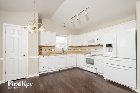 a kitchen with white cabinets and white appliances and wood floors