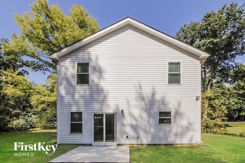 the front of a white house with a lawn and trees