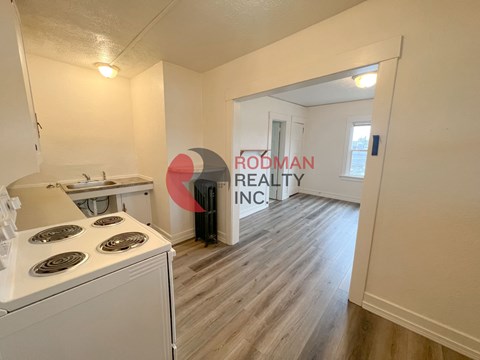 A small, clean, and empty apartment with a stove and a sign that says Rodman Realty Inc.