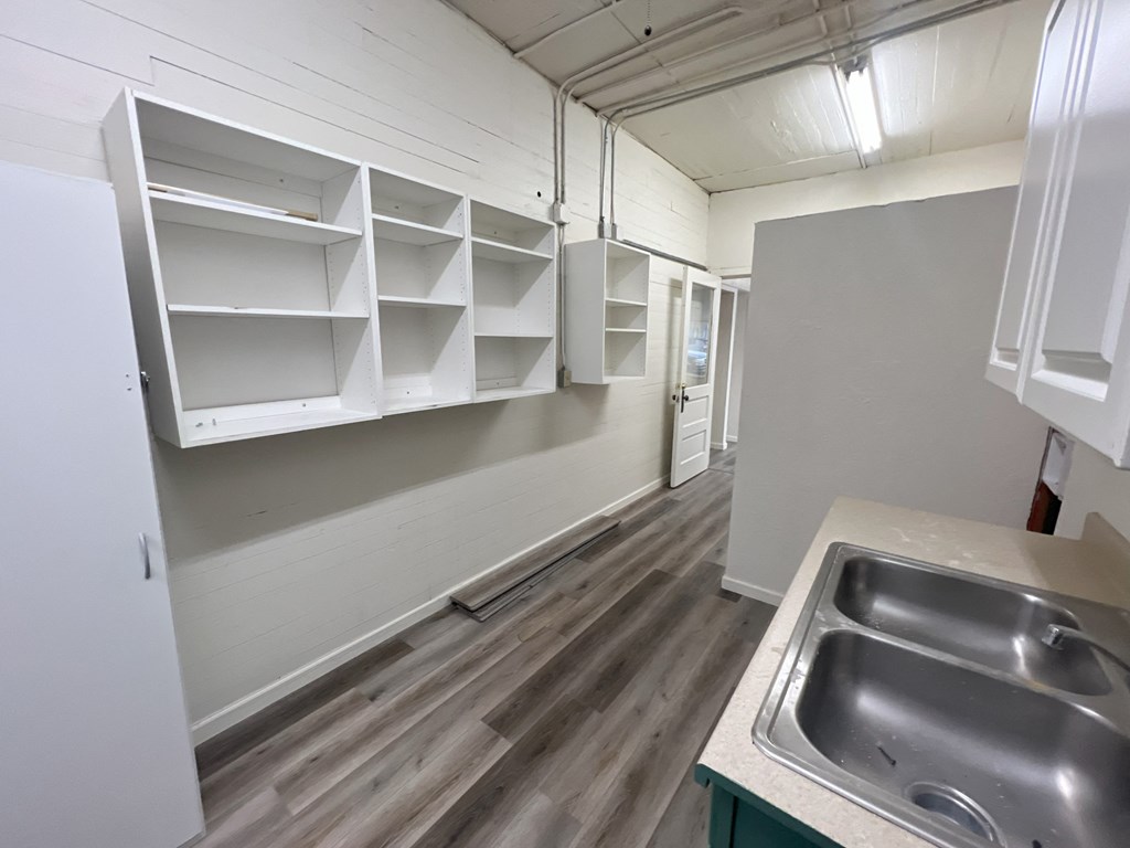 an empty room with a sink and a kitchen with white cabinets