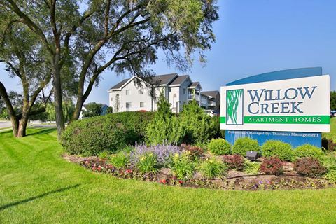 a sign for willow creek apartment homes in front of a garden