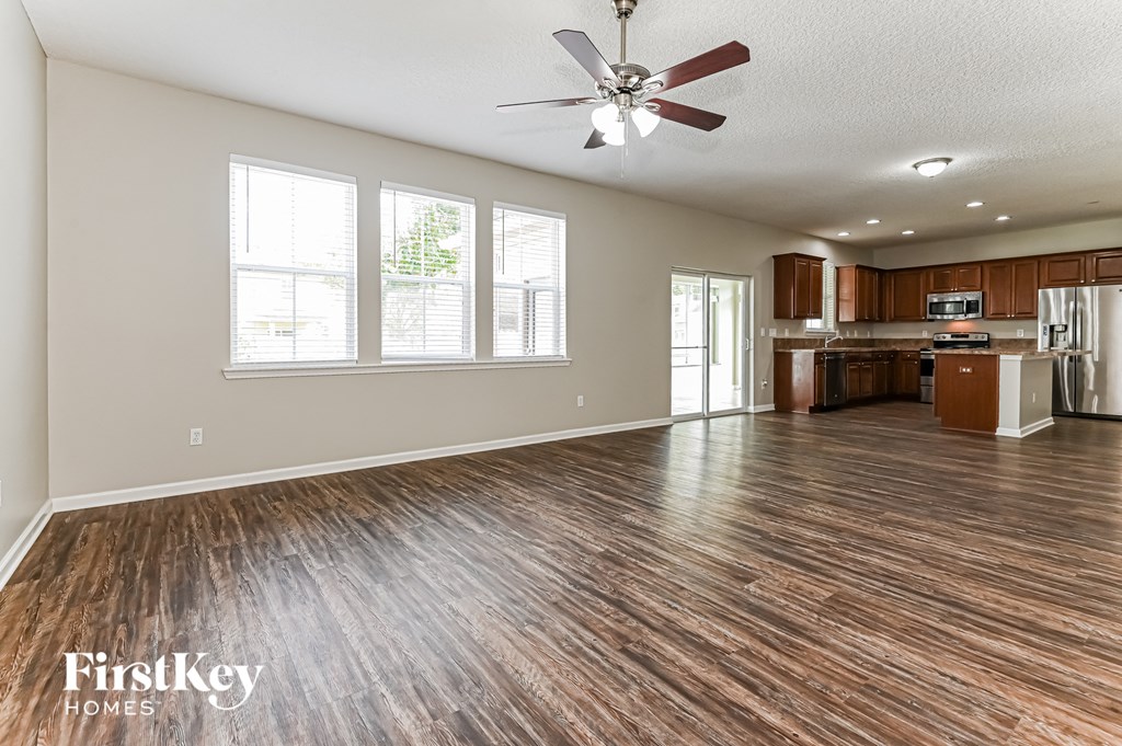 an empty living room with a ceiling fan and a kitchen