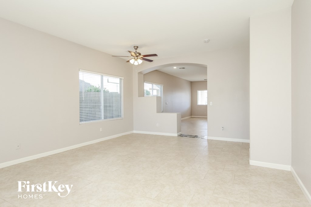 A spacious empty room with a ceiling fan and a window with blinds.