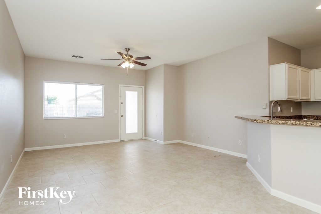 A spacious empty room with a ceiling fan and a window.