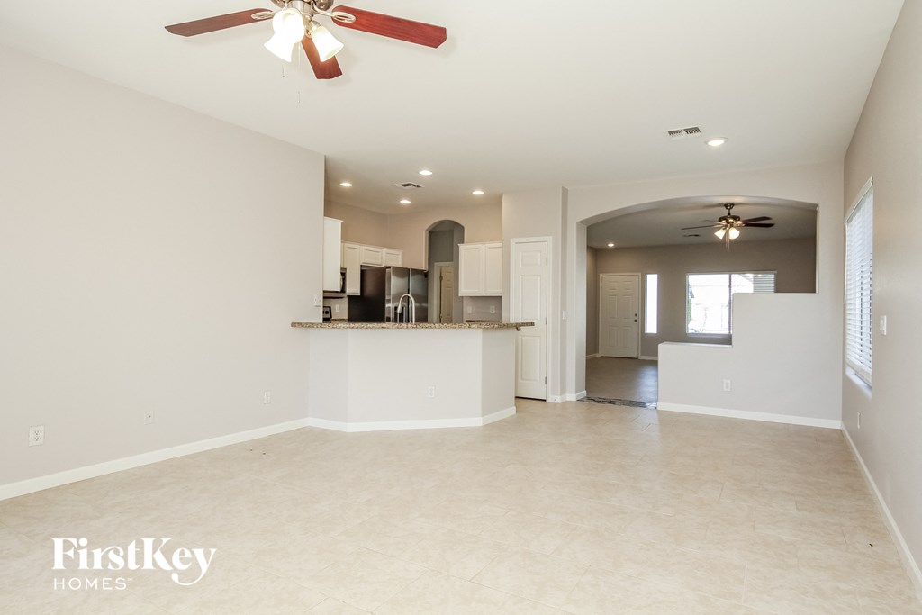 A spacious empty room with a red ceiling fan and a kitchen area in the background.