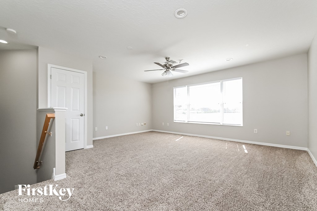 A spacious room with a carpeted floor, a ceiling fan, and a door leading to another room.