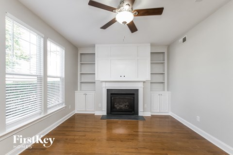 a living room with white shelves and a fireplace and a ceiling fan