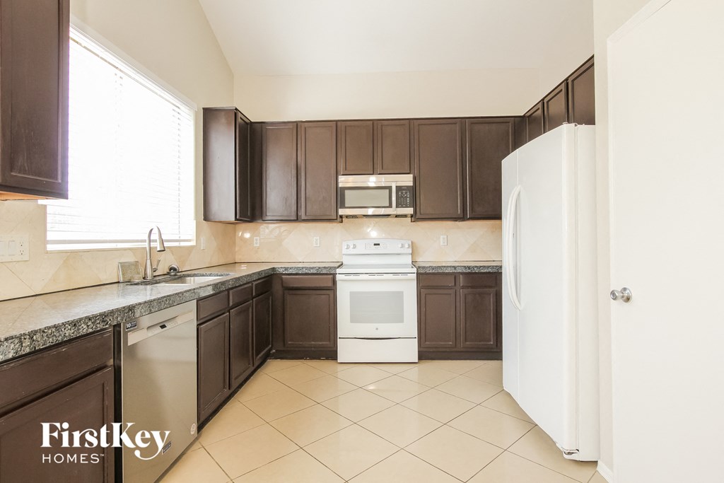 a kitchen with brown cabinets and white appliances and tiled floor