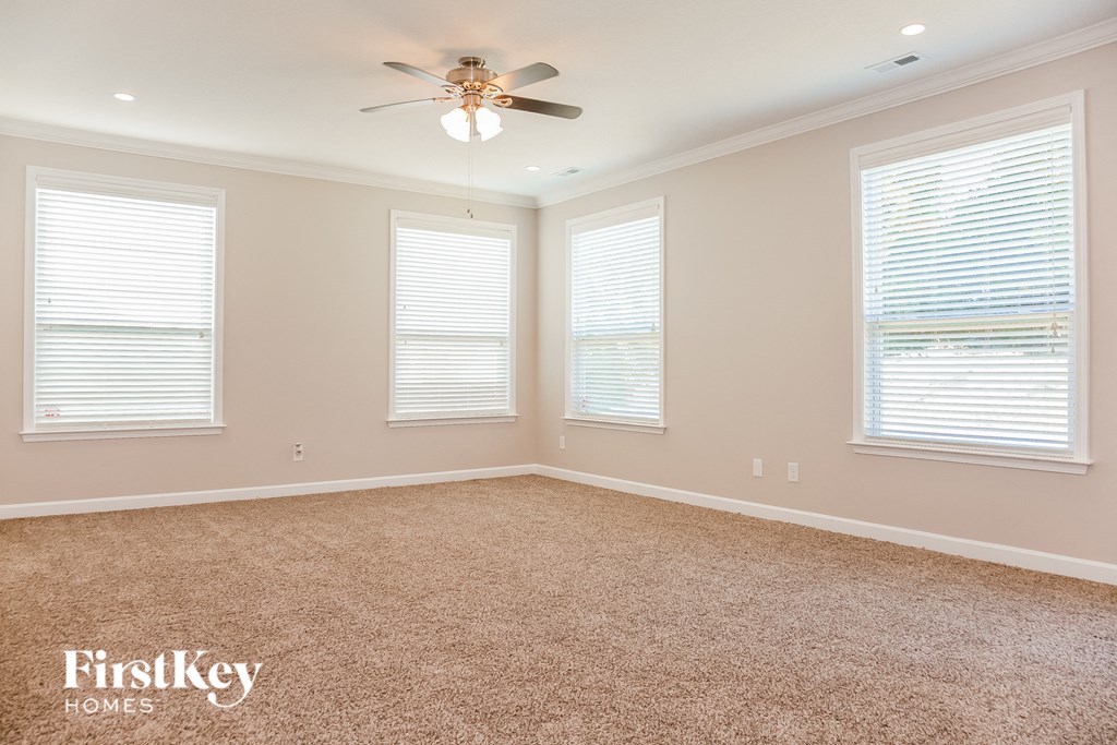 A room with a carpet floor, a ceiling fan, and three windows with blinds.