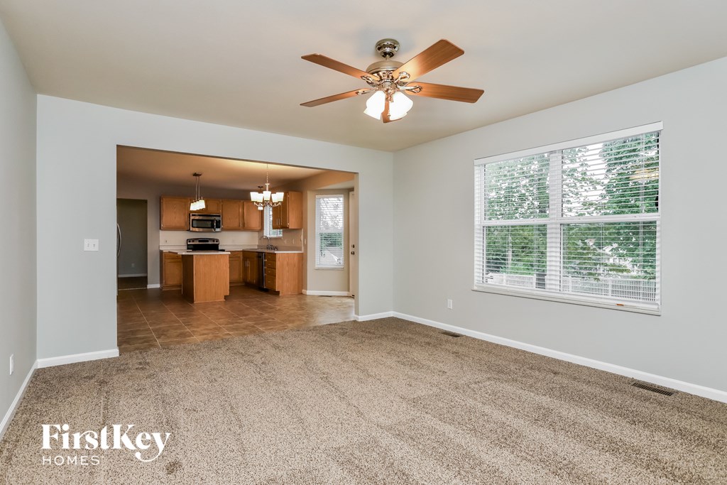 an empty living room with a ceiling fan and a kitchen
