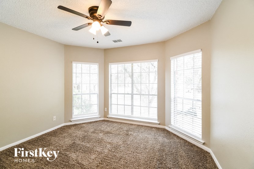 an empty living room with a ceiling fan and three windows