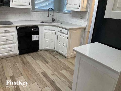 A kitchen with a black dishwasher and white cabinets.