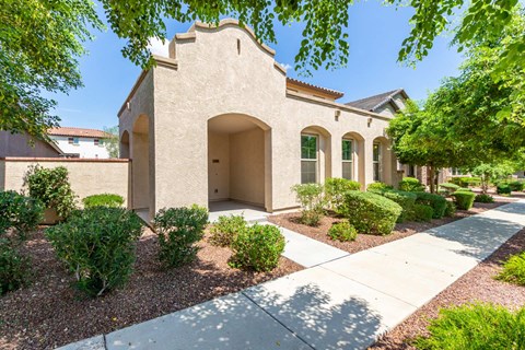 A beige building with arched windows and doors is surrounded by green shrubbery.
