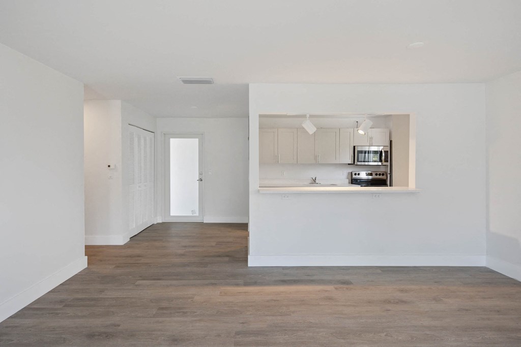 an empty living room and kitchen with white walls and wood floors