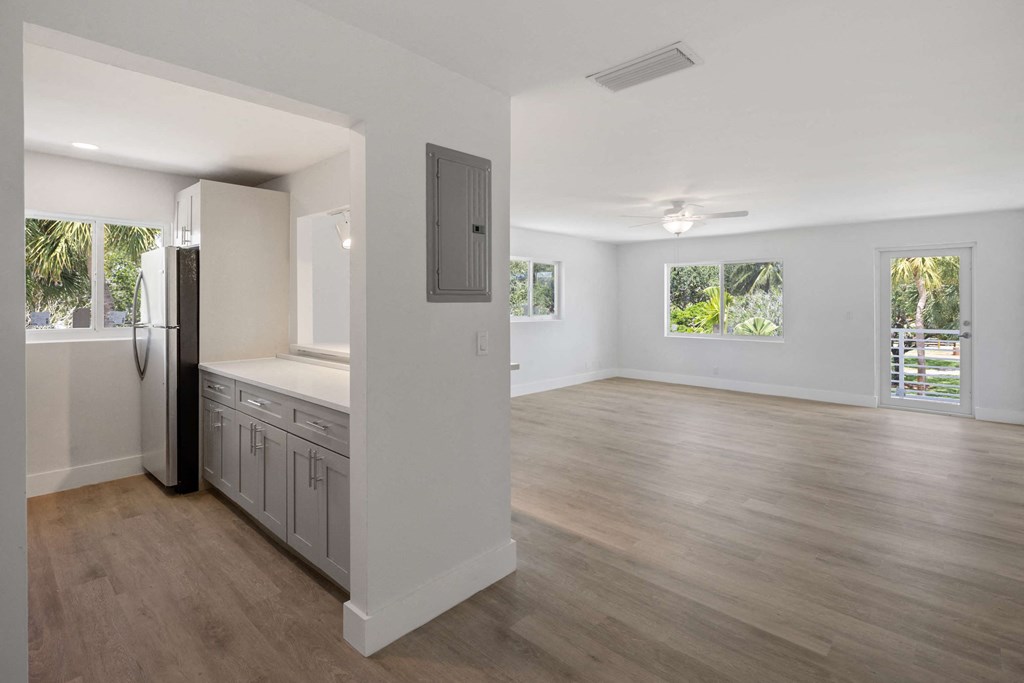 an empty living room and kitchen with a refrigerator and a window