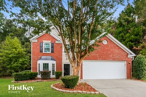 A red brick house with a white garage door and a tree in front.