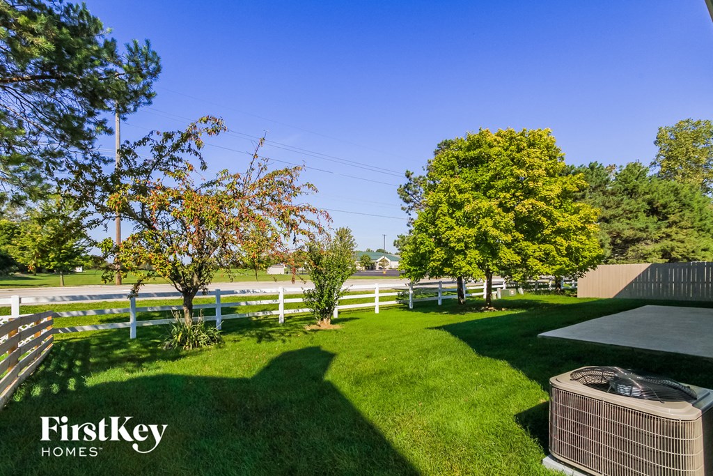 a backyard with a white fence and a grass lawn and a grill